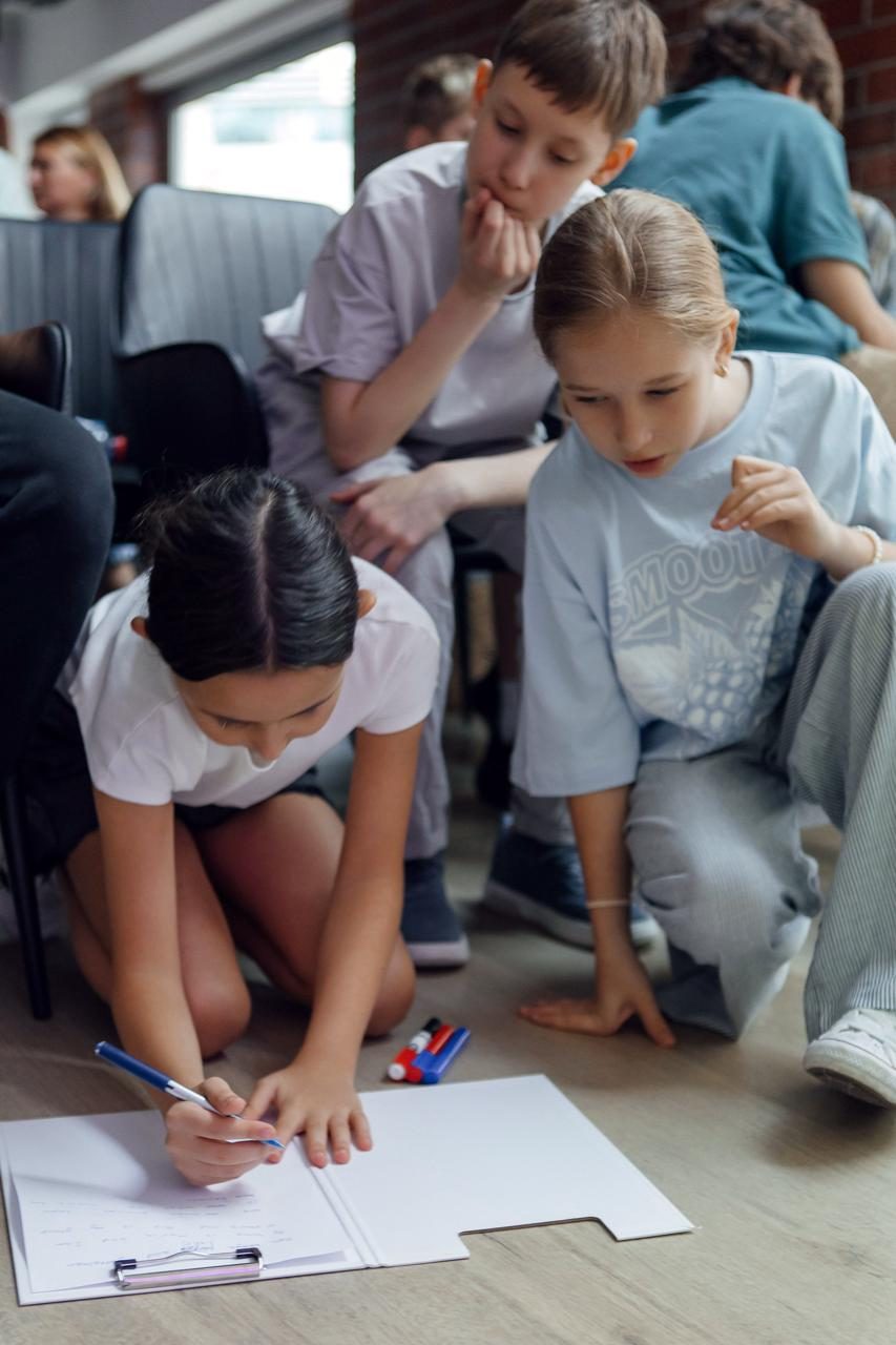 Children writing and drawing together on the floor at a Kidsology session